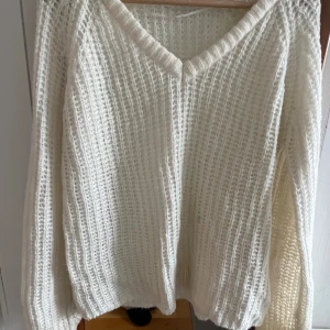 Vit stickad v-ringad tröja - Säljer en vit stickad tröja med v-ringad hals. Tröjan har en loose passform och är långärmad, perfekt för att hålla sig varm under kyliga dagar. Den grova stickningen ger en mysig och avslappnad vibe.