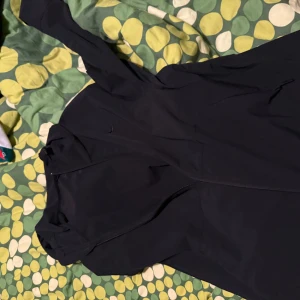 Svart vindjacka från Nike - Svart vindjacka från Nike med minimalistisk design och diskret logga på bröstet. Jackan har huva, långa ärmar och dragkedja framtill. Perfekt för dig som vill ha en clean look och gillar sportiga vibes.