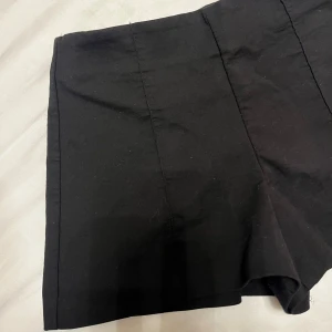Svarta kostym shorts från Zara - Snygga svarta shorts från Zara i storlek S med hög midja och stilrena sömmar. Modellen har raka ben och diskreta fickor bak. Materialet är mjukt och känns som bomull, perfekt för dig som gillar en clean och enkel look.