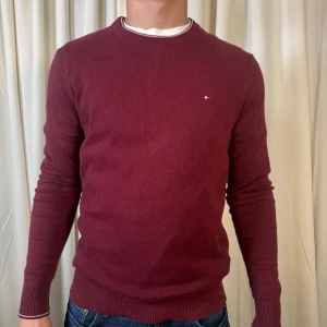 Vinröd tröja Tommy Hilfiger M - Snygg vinröd tröja från Tommy Hilfiger i mjuk pima bomull och kashmir. Klassisk rund hals, ribbade muddar och liten logga på bröstet. Perfekt för dig som gillar stilrena och bekväma plagg med premiumkänsla.