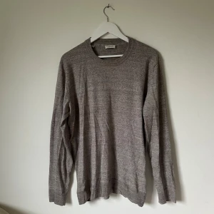 Beige stickad tröja från Selected Homme - En klassisk beige stickad tröja från Selected Homme i storlek XL. Tröjan har rund hals, ribbade muddar och långärmad passform. Perfekt för dig som gillar enkel och stilren design med mjukt material som känns skönt mot huden. 4F8