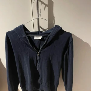 Mörkblå hoodie med dragkedja från Grunt - Mörkblå hoodie från Grunt i storlek L, med hel dragkedja framtill och huva. Tröjan har långärmade ärmar och är gjord i mjuk bomull. Perfekt för chill dagar och enkel att matcha med jeans eller joggers.