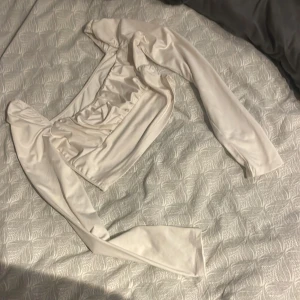 Vit långärmad croppad topp - Säljer en vit croppad topp med långa ärmar och rynkade detaljer framtill.