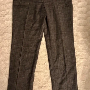 Grå rutiga kostymbyxor Rodebjer M - Snygga grå kostymbyxor från Rodebjer i storlek M. Byxorna har ett diskret rutmönster och är tillverkade i 100% ull för en lyxig känsla. Klassisk rak passform med midwaist och fickor fram. Perfekta för en stilren look.  Ett pyttelitet hål (1mm ) på baksidan av byxan som en hängig kan lätt åtgärda, i övrigt jättebra skick