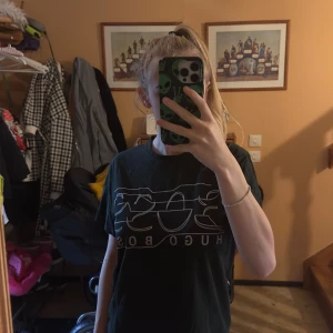 Svart Hugo Boss t-shirt med tryck - Svart t-shirt från Hugo Boss med stort vitt tryck på bröstet. Klassisk rund hals och korta ärmar. Materialet känns mjukt och lätt, perfekt för dig som gillar stilrena logotoplagg. Snygg passform som funkar till jeans eller shorts.