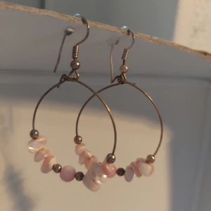 Hoopörhängen med rosa pärldetaljer - Stilrena hoopörhängen med tunna metallringar och ljusrosa pärlor i olika former. Pärlorna är mixade med små metallkulor för en cool och unik look. Perfekta för dig som gillar boho-vibbar och vill ha något som sticker ut lite extra.