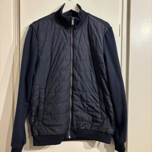 Blå cardigan från Bläck, stl S - Tjena! Jag säljer min stilrena blå cardigan från Bläck i storlek S. Jackan har quiltad framsida i syntetmaterial, släta ärmar och ribbade muddar. Dragkedja framtill och två fickor. Perfekt för dig som gillar minimalistisk och modern stil. Cardiganen har ett litet ihopsytt hål under dragkedjan som syns på bild 5 men det är inget som syns när du har på dig den. Skick: 7/10. Bara att ställa frågor om det är något!😊 Priset är inte hugget i sten!😀 mvh