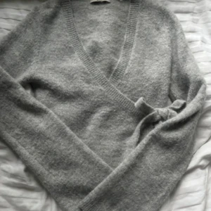 Stickad omlottröja gina - Superfin stickad omlotttröja i ljusgrått från Gina! Storlek S och sparsamt använd. Färgen är något ljusare än på bilden! Den är lite tunnare stickad, vilket passar perfekt till alla årstider samt till både vardagligare och festligare tillfällen! SLUTSÅLD! Bara att höra av dig vid frågor!🤍