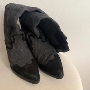 Svarta cowboy boots från Zara - Säljer ett par svarta cowboy boots från Zara med spetsig tå och låg klack. Bootsens ovandel är i textil med snygga broderade detaljer och mocka-liknande partier. De har en klassisk westernform och är perfekta för dig som vill sticka ut med din stil.