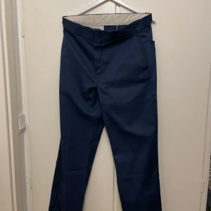  Dickies 874 chinos - Säljer ett par klassiska mörkblå Dickies 874 chinos med raka ben och normal passform. Byxorna har fickor både fram och bak, samt Dickies-logga ovanför bakfickan. Materialet är en slitstark mix av polyester och bomull.