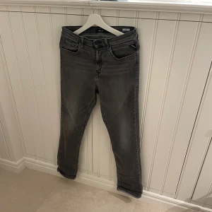 Replay grå jeans med raka ben - Snygga grå jeans från Replay med klassisk femficksdesign och raka ben. Jeansen har svarta detaljer vid fickorna och en diskret Replay-logga. Materialet är mjukt jeans och färgen är en cool mörkgrå ton med lätt tvättad look.