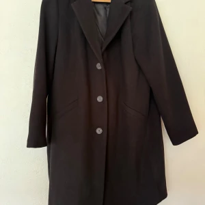 Svart kappa från Vero Moda - Svart kappa från Vero Moda med klassisk krage och tre stora knappar framtill. Jackan har två snedställda fickor och är helfodrad. Långärmad och rak passform, perfekt för dig som gillar stilrena och tidlösa plagg. Materialet är mjukt och känns skönt mot kroppen. Oanvänd, har bara hängt i garderoben sedan köpet.  Ordinarie pris ca 650kr