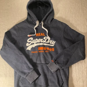 Mörkblå Superdry hoodie med tryck - | märke: Superdry | plagg: Hoodie | skick: 9/10 | storlek: L | nypris: 1500kr | mitt pris: 349kr | färger: mörkgrå | pris kan diskuteras | hör av dig vid minsta fråga eller fundering // LeClosMatteo