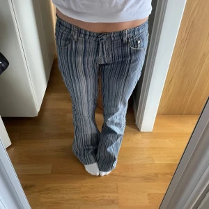 Randiga bootcut jeans i blått - Säljer ett par blå och vita randiga jeans  med bootcut passform. Byxorna har låg midja, klassiska fem fickor och är gjorda i jeansmaterial. Snygga kontrastsömmar och coolt mönster som sticker ut. Perfekta för dig som vill ha en unik look.