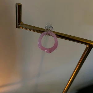 Rosa chunky örhänge i plast - Säljer ett coolt örhänge i chunky stil, gjort i genomskinlig rosa plast. Örhänget har en rund, något kantig form och fästs med en transparent clip-on. Perfekt för dig som vill sticka ut med färg och form.