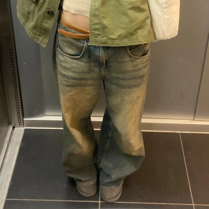 Baggy blå jeans med låg midja - Säljer ett par baggy blå jeans med låg midja och breda ben. Jeansen har klassisk femficksdesign och slitna detaljer för en cool, avslappnad look. Perfekta för dig som gillar streetstyle och vill ha en skön passform.