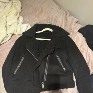 Svart teddyjacka med dragkedjor - Svart teddyjacka från stradivarius med grov krage och detaljer i teddytyg. Jackan har två sneda dragkedjefickor och en kraftig dragkedja framtill. Croppad modell med breda muddar i teddy och cool streetstil. Perfekt för dig som gillar oversized look.