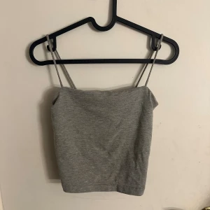 Grå linnetopp från Gina Tricot - Säljer en enkel och stilren grå linnetopp från Gina Tricot i storlek S. Toppen har smala axelband och ärmlös design, perfekt för varma dagar. Materialet är mjukt och stretchigt, vilket gör den skön att bära. Passformen är normal och toppen är enfärgad utan detaljer.