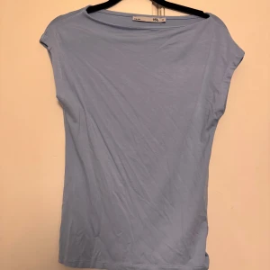 Ljusblå topp från lager 157 XS - En skön ljusblå topp från lager 157 i modellen 'Livia'. T-shirten har en enkel, ärmlös design med rundad hals och mjukt material som känns bekvämt mot huden. Perfekt att styla med jeans eller kjol för en clean look.