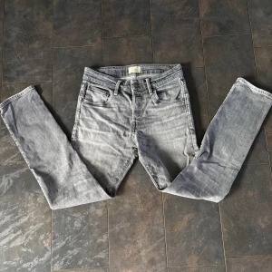 Jack and Jones jeans  - Snygga grå jeans från Levi's med klassisk femficksdesign och smal passform. Jeansen har en cool tvättad look, raka ben och normal midja. Perfekt för dig som gillar en stilren och modern vibe. Materialet är mjukt jeans och de har knappar och dragkedja framtill. Lite sliten på ena sidan men inget man bryr sig om