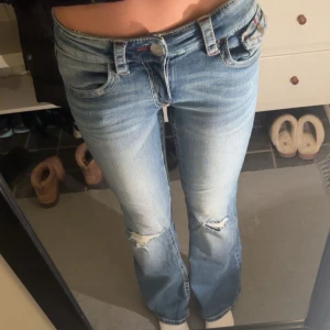 Gina tricot bootcut jeans med broderi - Snygga blå bootcut jeans från Gina tricot Young 14+ med slitningar på knäna och coolt rött broderi på bakfickorna. Klassisk femficksmodell, låg midja och detaljerade sömmar. Perfekt för dig som gillar en avslappnad och trendig stil. (Jag är 165 cm). Endast använda en gång. 