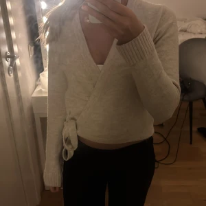 Beige omlottkofta från Kappahl - Supermysig beige omlottkofta från Kappahl med knyt i sidan och ribbade muddar. Koftan är stickad och har lång ärm, perfekt för lager-på-lager och chill dagar. Snygg v-ringning.