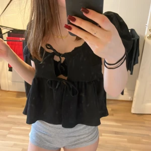 Svart blus med puffärm från Gina Tricot - Supersöt svart blus från Gina Tricot i storlek XS. Modellen har puffärmar, två knytningar framtill och en flowy, luftig passform. Tyget är lätt och har en diskret struktur som ger extra känsla. Perfekt att styla med jeans eller kjol för en trendig look.