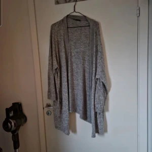 Gråmelerad kofta i mjukt material - Lång kofta som är gråmelerad och har fickor. Fint skick bara använd ett par gånger. Katt finns i hemmet