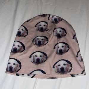 Beige mössa med hundmotiv - Säljer en beige mössa med tryck av söta hundansikten över hela tyget. Mössan är mjuk och stretchig, perfekt för att hålla värmen. Passar dig som vill sticka ut med en unik accessoar och älskar hundar.