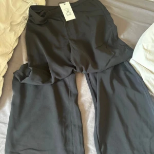 Vida svarta kostymbyxor - Snygga svarta kostymbyxor med vida ben och petit modell. Perfekta för en clean och stilren look. Byxorna har en slät front och är gjorda i ett mjukt, lätt material som ger en skön känsla hela dagen.