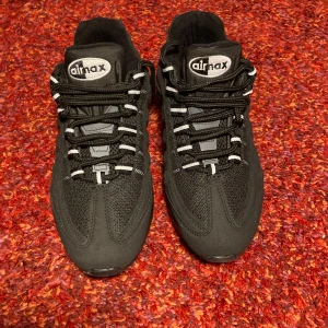 Svarta Nike Air Max 95 sneakers - Säljer ett par svarta Nike Air Max sneakers med klassisk chunky sula och synliga luftbubblor. Skorna har mesh och syntetmaterial i ovandelen, svarta snören med vita detaljer och rund tå. Perfekta för dig som gillar streetwear och sportig stil.