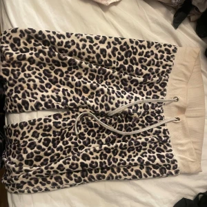 Leopardmönstrade mjukisbyxor i beige - Leopardmönstrade mjukisbyxor i beige och svart med bred resår och snörning i midjan. Byxorna har muddar vid bensluten och är tillverkade i ett mjukt material som känns skönt mot huden. Perfekta för en chill och avslappnad stil. 