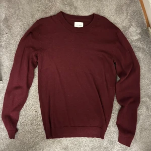 Vinröd tröja i merinoull A Day's March - Vinröd tröja från A Day's March i 100% fin merinoull. Klassisk rund hals och långärmad modell med ribbade muddar vid ärmslut och nederkant. Perfekt för dig som gillar stilrena och mjuka plagg med snygg passform. Storlek S