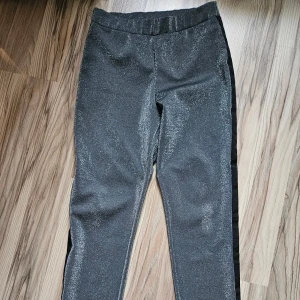 Glittriga svarta byxor Gina Tricot M - Snygga svarta byxor från Gina Tricot i storlek M med glittrig finish och svarta sidopaneler. Byxorna har en smal passform och resår i midjan för extra komfort. Perfekta för dig som vill sticka ut med en cool look.