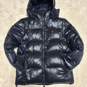 Mörkblå Vinterjacka från Polo Ralph Lauren - Mörkblå vinterjacka från Polo Ralph Lauren med luva och röd logga på bröstet. 