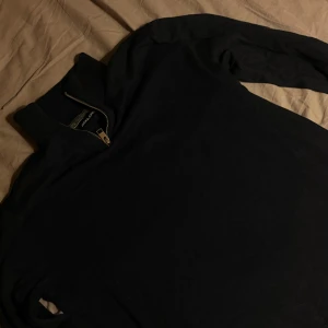 Svart half zip tröja Jack & Jones - Svart långärmad tröja från Jack & Jones med hög krage och snygg half zip-dragkedja i metall. Tröjan är stickad och har en clean look som passar perfekt till jeans eller chinos.