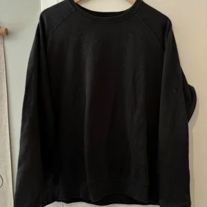Svart sweatshirt från 157  - En enkel svart sweatshirt från 157 i storlek XL. Tröjan har rund hals, långa ärmar och är tillverkad i mjuk bomull. Perfekt för chill dagar eller när du vill ha en clean look. Snygg att matcha med jeans eller joggers. Använd men i mycket bra skick