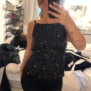 Svart glittrig linnetopp med öppen rygg - Säljer en svart glittrig linnetopp med smala axelband och öppen rygg. 