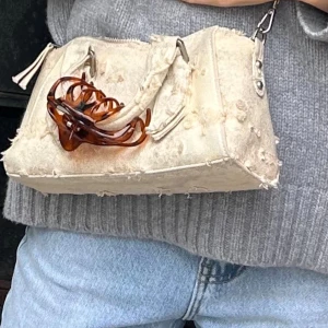 Beige handväska med kedja - Cool beige handväska i canvas med slitna detaljer och råa kanter. Väskan har både handtag och en axelrem i metallkedja samt dragkedja upptill. Perfekt för dig som gillar en edgy och unik stil.