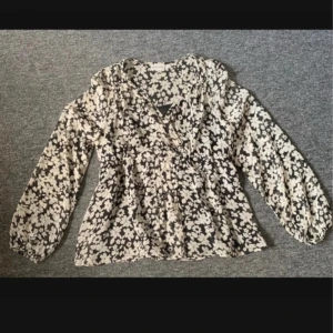 Blommig svartvit blus från Cappuccini - Säljer en blommig blus från Cappuccini i svart och vitt. Blusen har långärmade puffärmar, v-ringad hals och är tillverkad i ett lätt, transparent material med svart innerlinne. Perfekt för dig som gillar detaljer och mönster! Aldrig använd!