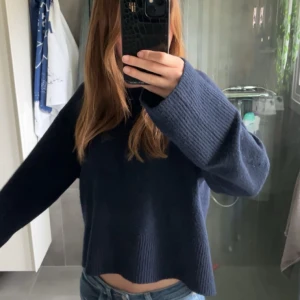 Mörkblå stickad tröja med vida ärmar - Säljer en mörkblå stickad tröja med croppad passform och vida, långa ärmar. Perfekt för dig som gillar en chill och oversized stil. Tröjan är enkel men ändå snygg och passar till allt. Är lite luddrig efter tvättar.