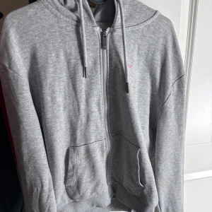 Grå hoodie från FILA med dragkedja - Säljer en grå hoodie från FILA i storlek S. Tröjan har huva med snörning, två fickor fram och hel dragkedja. Diskret FILA-logga på bröstet och metalländar på snörena 