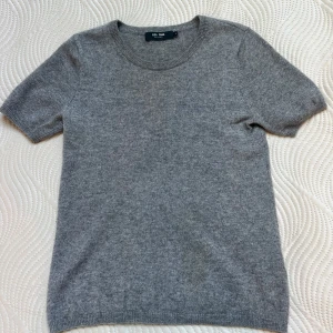 Grå kashmirtröja från Lisa Yang - Superskön grå tröja i 100% kashmir från Lisa Yang. Rund hals och korta ärmar. Tröjan har en klassisk passform och ribbade kanter vid hals, ärmslut och nederkant.