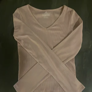 Beige ribbad långärmad topp H&M - Säljer en beige ribbad långärmad topp från H&M i storlek 146/152. Toppen har v-ringad hals och är tillverkad i ett mjukt, stretchigt material som sitter snyggt på kroppen. Perfekt att styla med jeans eller kjol för en clean look.