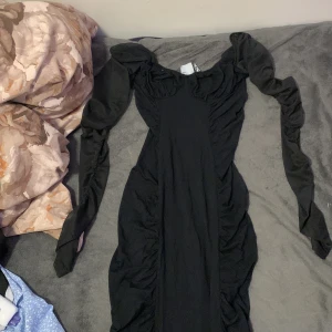 Svart långklänning från ASOS DESIGN - Supersnygg svart långklänning från ASOS DESIGN med puffiga långärmar och rynkade detaljer längs sidorna. Klänningen har en figurnära passform och är tillverkad i mjukt material som känns bekvämt mot huden. Perfekt för dig som vill sticka ut med en dramatisk siluett. Den ser konstigt ut men när du tar på dig den så är den jätte fin och man får kurvor jag vill inte ha den för att den passar inte mig har inte använt nån gång 