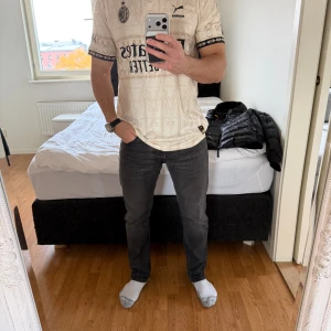 AC Milan x Puma  fotbollströja - AC Milan fotbollströja i beige med svarta detaljer från Puma. Snyggt mönster över hela tröjan, svart krage och loggor på bröstet. Materialet är lätt och andas, perfekt för match eller träning. Tryck med Emirates och wefox.