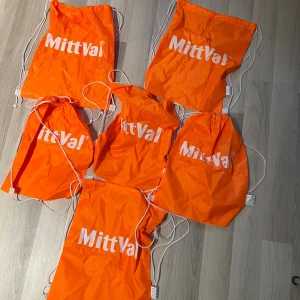 Orange gympapåsar från MittVal - Säljer flera orangea gympapåsar från MittVal med vitt tryck och vita snören. Perfekt för att bära träningskläder eller skor. Väskorna är lätta och smidiga att ta med sig överallt.