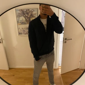 Mörkblå quiltad bomberjacka J.Lindeberg - Snygg mörkblå cardigan från J.Lindeberg med quiltad framsida och stickade ärmar. Jackan har dragkedja framtill och en cool ficka på ärmen. Perfekt för dig som vill ha en stilren och modern look.