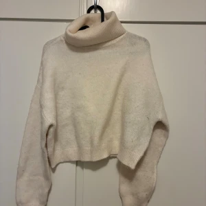 Ljusbeige croppad polotröja - Supermysig ljusbeige polotröja med croppad passform och bred krage. Tröjan har långa ärmar och är stickad i ett mjukt material som känns skönt mot huden. Perfekt för att hålla sig varm och ändå se chill ut.