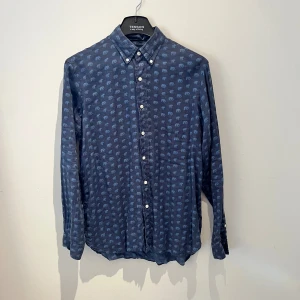 Blå skjorta med elefantmönster Ralph Lauren - Snygg vintage blå skjorta från Ralph Lauren med unikt elefantmönster över hela plagget, den är minst 20 år gammal och är nästan aldrig använd. Skjortan har klassisk krage, vita knappar framtill och långa ärmar med knapp vid manschetten. Tillverkad i linne blandning med bomull som känns skönt mot huden.